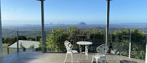 Een overdekt terras met een tafel en stoelen, met uitzicht op een schilderachtige omgeving met bergen en groen.