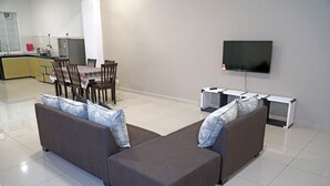 A modern living room with a sectional sofa, a dining area with chairs, a flat-screen TV mounted on the wall, and a kitchen in the background. - CVR Homestay Melaka (Jasin)