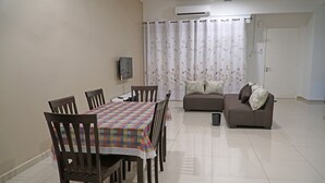 A dining area with a table and chairs, a sofa, and a television. - CVR Homestay Melaka (Jasin)