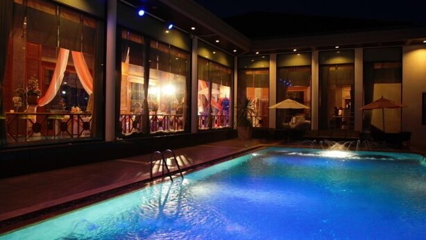 A swimming pool with a water feature, surrounded by a covered outdoor area with tables and umbrellas. - S.D. Avenue Hotel (Bangkok)