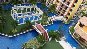 Un hôtel à plusieurs étages doté d’une cour intérieure où se trouve une piscine, le tout entouré d’une végétation luxuriante et agrémenté d’un pont décoratif.
