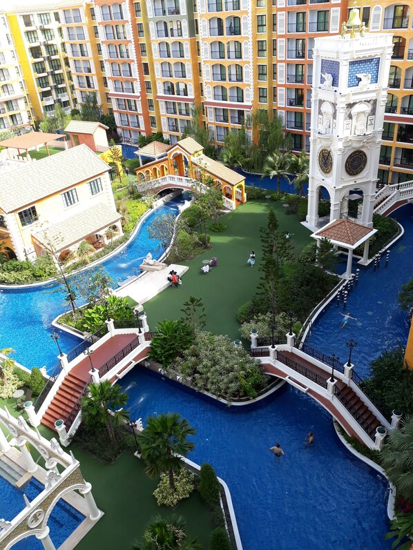 Un resort con varias piscinas, una fuente central y una torre de campanas.