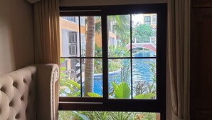Une fenêtre donnant sur une piscine, des palmiers et un pont.