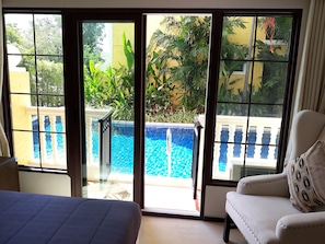 Una habitación con cama, un sillón blanco y vista a una piscina a través de un ventanal.