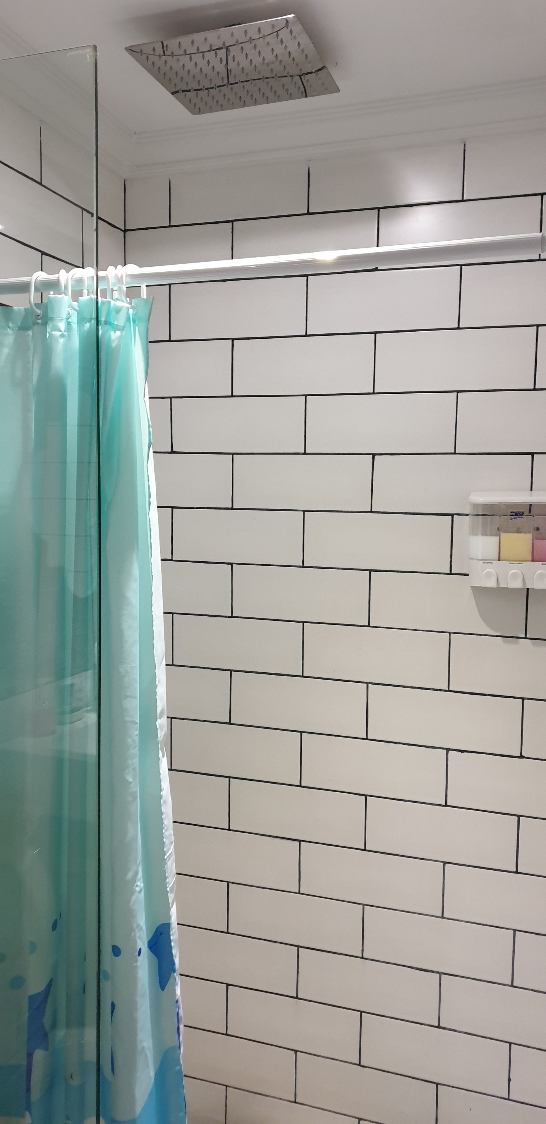A bathroom with a shower curtain, white tiled walls, and a small shelf with toiletries.