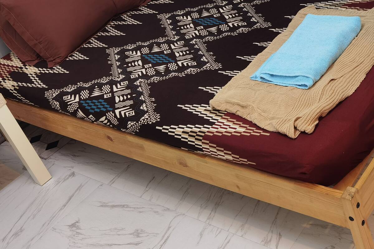 Un lit avec une couvre-lit à motifs, une serviette bleue et un plaid beige.