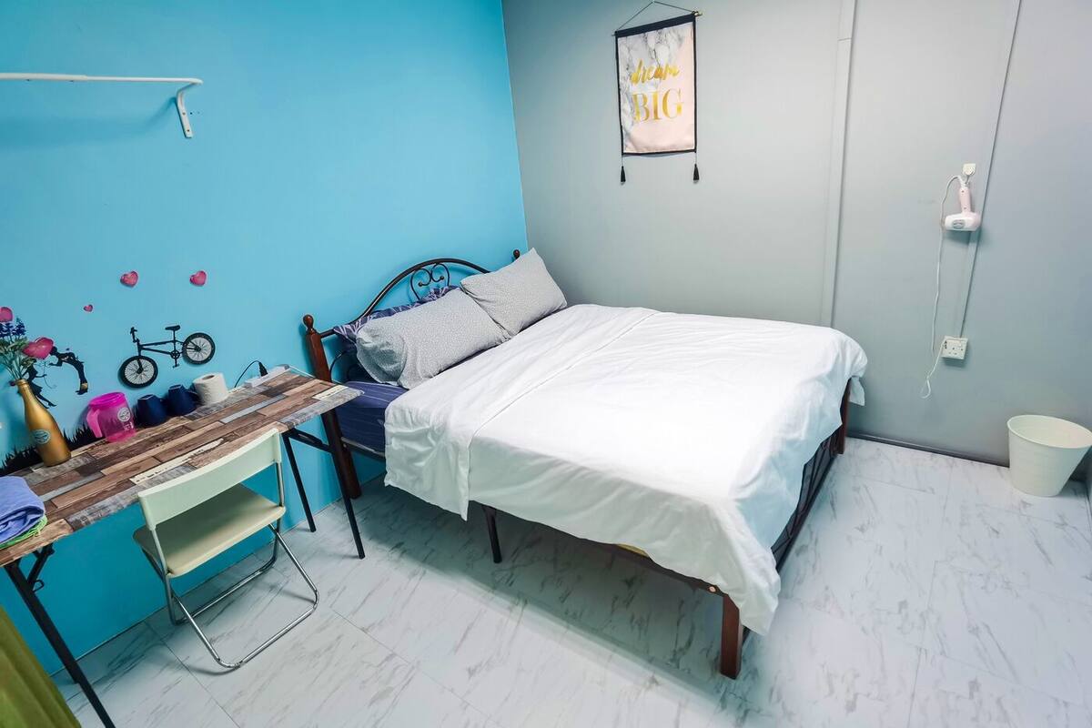 Une chambre à coucher avec un lit, un bureau et une chaise. Il y a un élément de décoration murale et une prise électrique.
