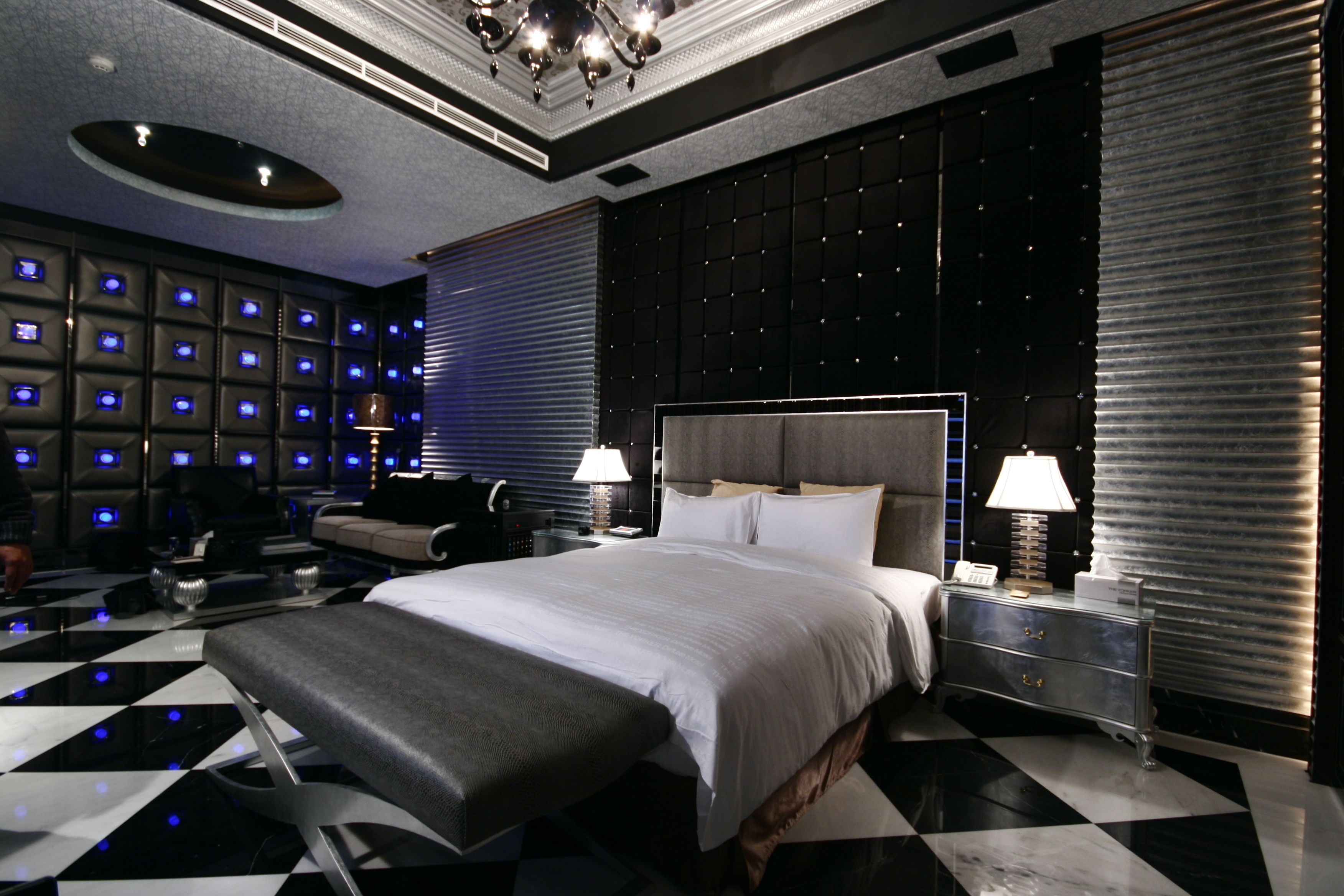 Een moderne slaapkamer met een groot bed, een bankje, een bureau en een wand met verlichte schermen.