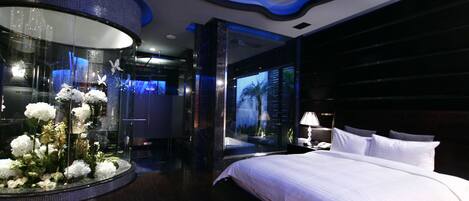 A modern hotel room with a large bed, a glass display with flowers, and a cityscape view.