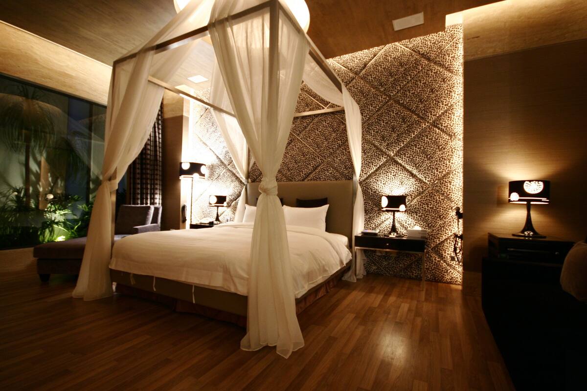 A bedroom with a four-poster bed, wooden flooring, and patterned wallpaper.