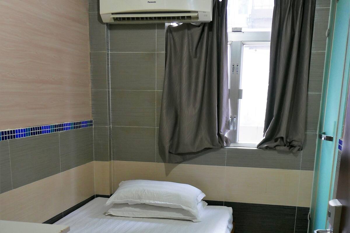 A hotel room with a bed, a window with curtains, an air conditioner, and a door.