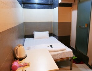 A small, compact hotel room with a single bed, a bedside table with a hairdryer and a remote control, and a door with a 'pull' sign. - KK Hotel (Kowloon)