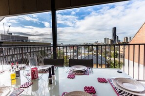A dining area with a table set for two, overlooking a cityscape with buildings and a clear sky. - Carrington Manor (Spring Hill)