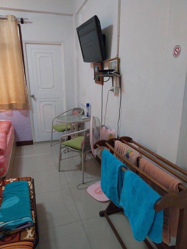 Una habitación con una cama, una silla, una mesita, un televisor montado en la pared y un banco de madera con toallas.