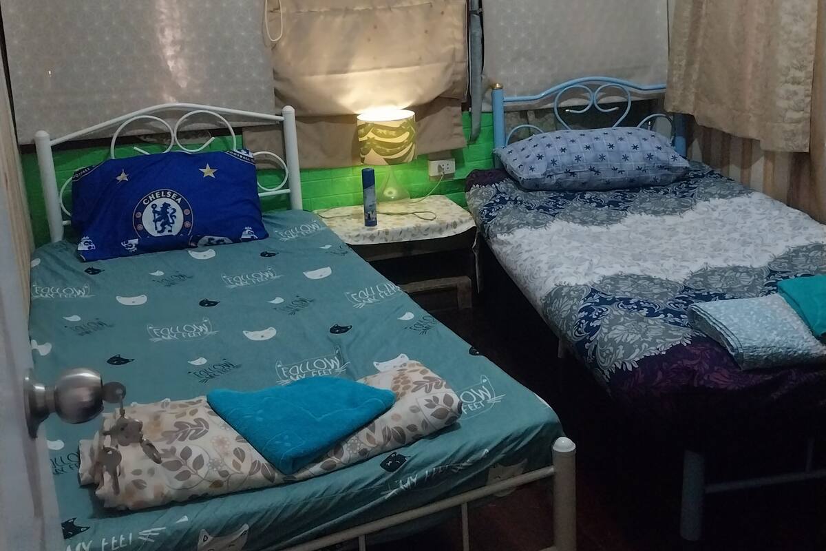 Una habitación pequeña y acogedora con dos camas individuales, una mesita de noche con lámpara y un equipo de aire acondicionado.