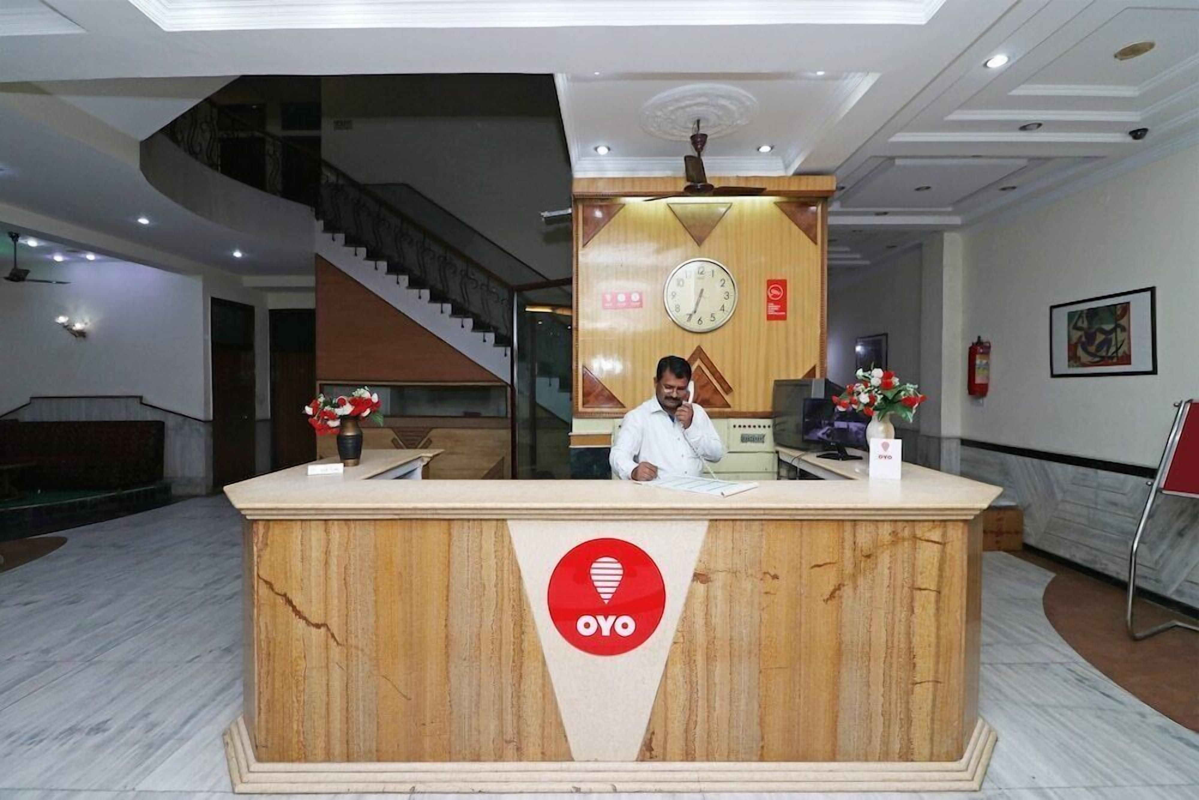 A reception desk with a wooden finish and a logo, a clock, and a staircase in the background.