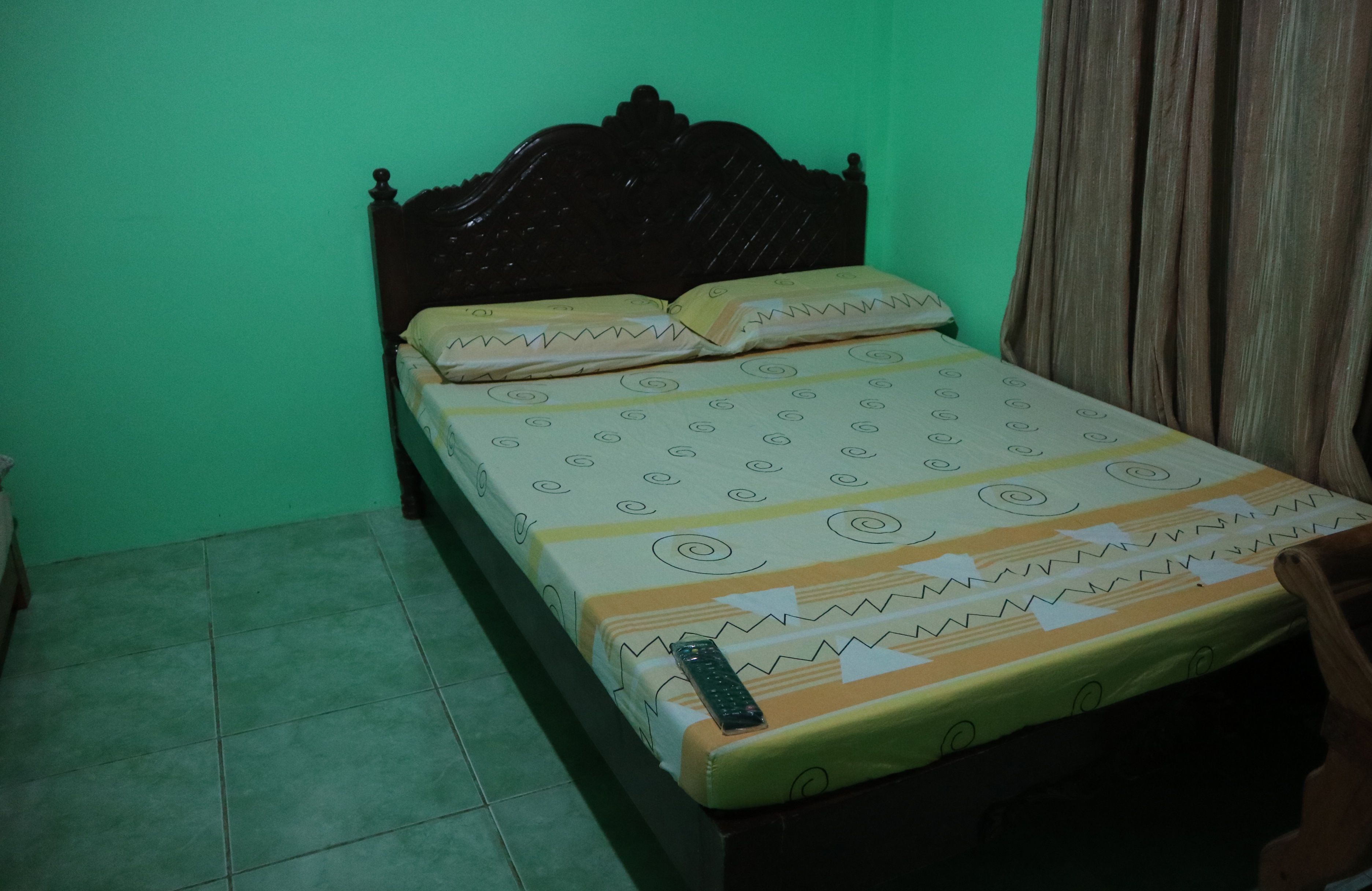 Ein Bett mit einem gemusterten Überwurf, einer Fernbedienung auf dem Bett und einem Holzkopfende.