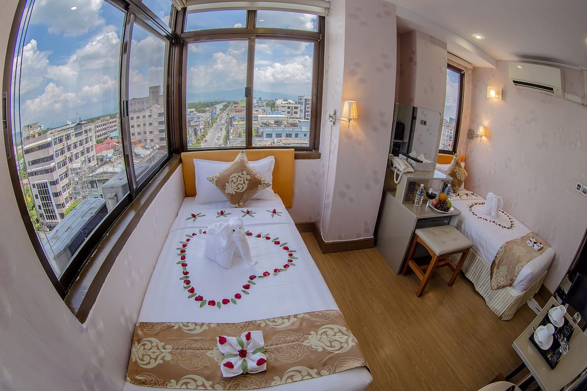 Habitación de hotel con un ventanal grande, una cama con almohada decorativa, una mesita de noche con lámpara y un escritorio pequeño con teléfono.