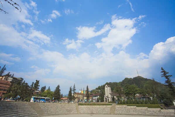 A public square with steps leading up to a hill, a church, and a bus in the background.