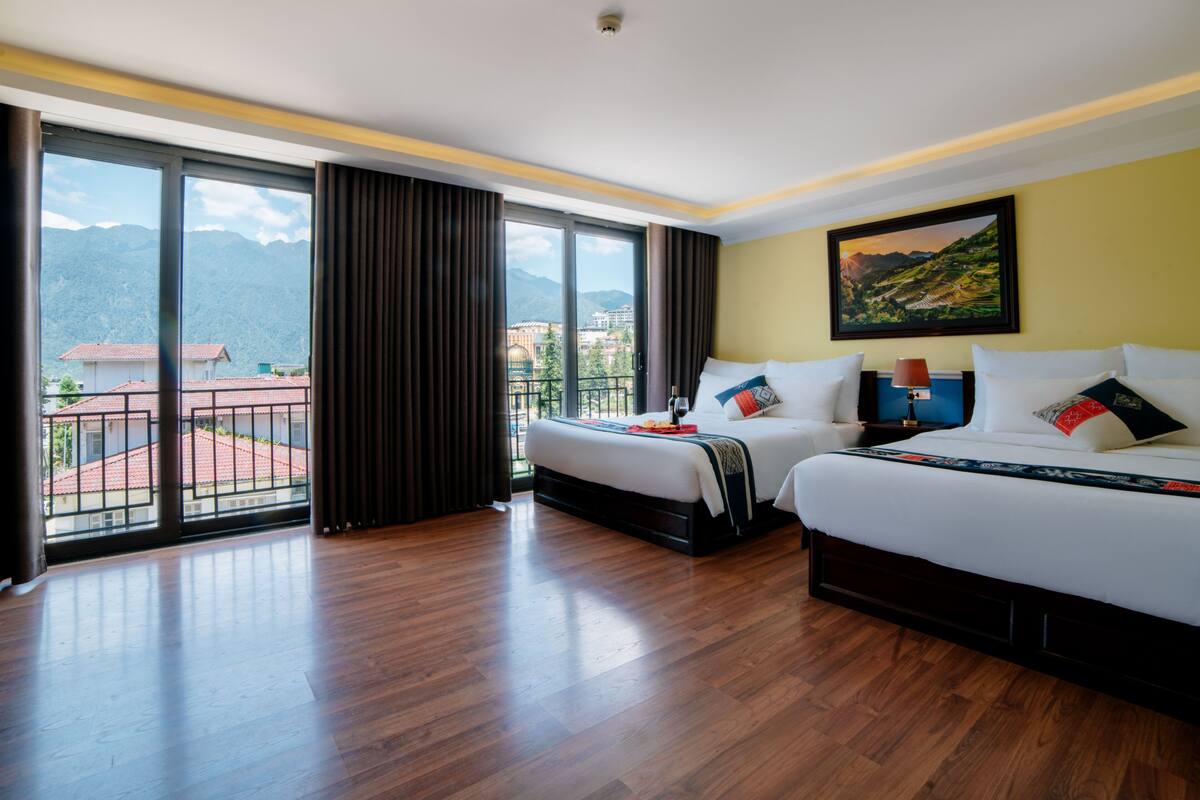 A hotel room with two beds, a large window with a view of mountains, and a painting on the wall.