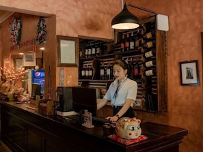 Zona de bar con mostrador, una persona detrás del mostrador y estantes con botellas.