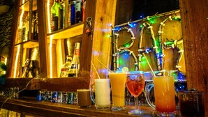 Un bar con diversas bebidas y botellas, estantes de madera y luces de colores.