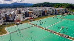 A residential complex with multiple apartment buildings, a central green sports court, and a mountainous backdrop. - Quin Homestay (Kota Kinabalu)