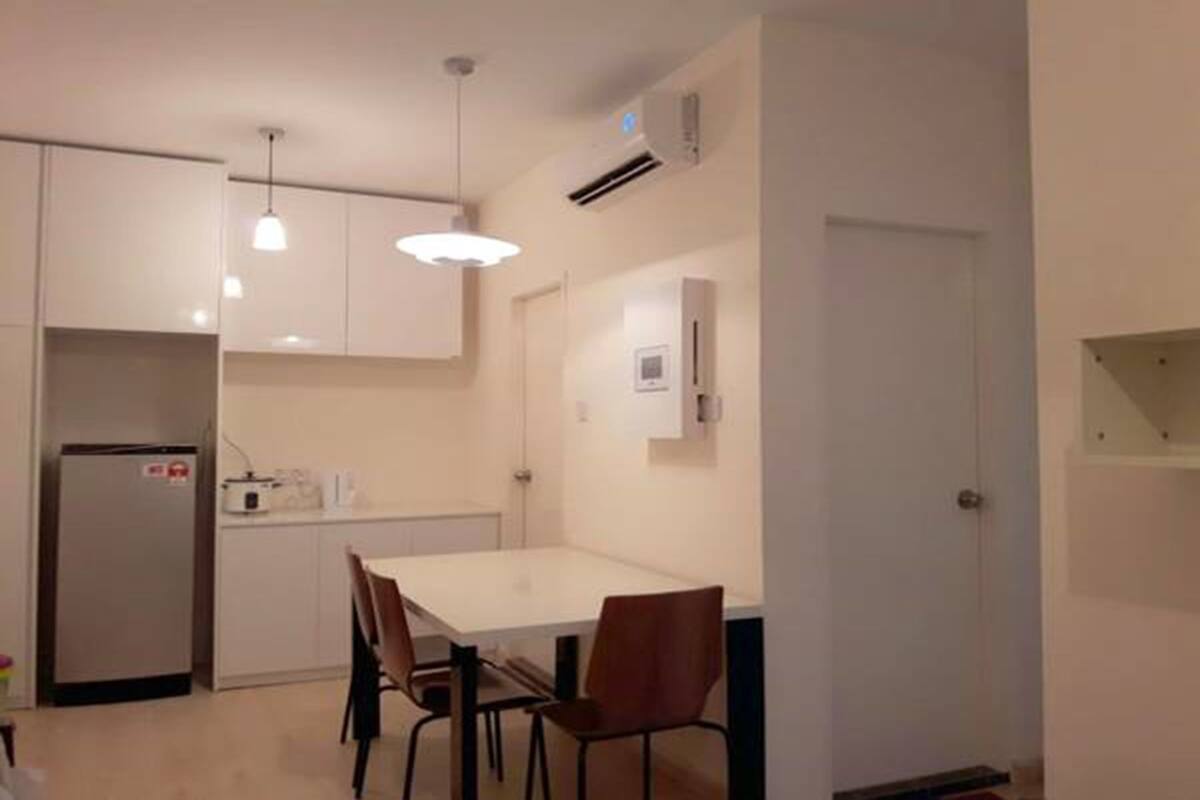 Une cuisine compacte avec des meubles blancs, un réfrigérateur, une table à manger avec des chaises, des luminaires suspendus et une petite fenêtre.