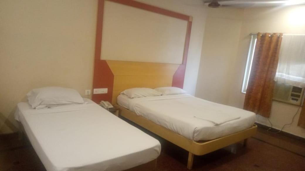 A room with two single beds, a wooden headboard, a telephone, and a window with curtains.