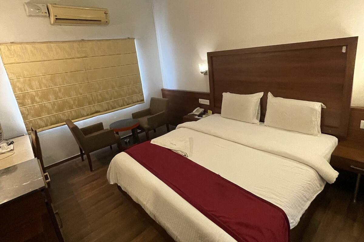 Habitació d'hotel amb un llit gran, un escriptori, una cadira, una taula petita i una unitat de aire condicionat a la paret.