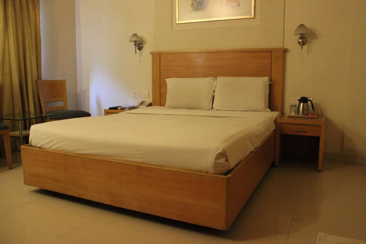 Habitació d'hotel amb un llit de fusta, dues taules de nit, una cadira, un escriptori i una làmpada.