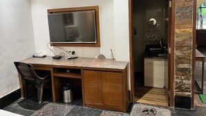 Un espace de bureau compact comprenant un bureau en bois, un grand miroir et une petite kitchenette.