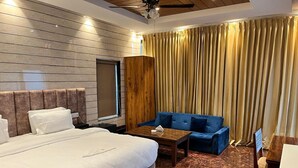 Une chambre d’hôtel avec un grand lit, un canapé bleu, une armoire en bois et une moquette à motifs.