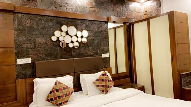 Une chambre avec un mur en pierre, une tête de lit en bois et un lit avec une literie blanche et des coussins à motifs.