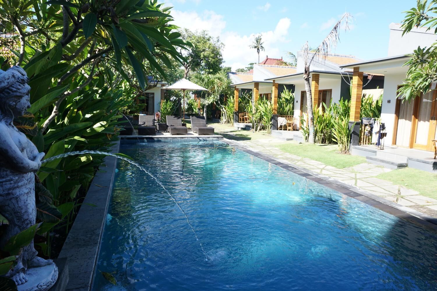 A swimming pool with lounge chairs and umbrellas, surrounded by greenery and buildings.