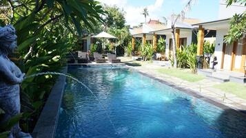A swimming pool with lounge chairs and umbrellas, surrounded by greenery and buildings.