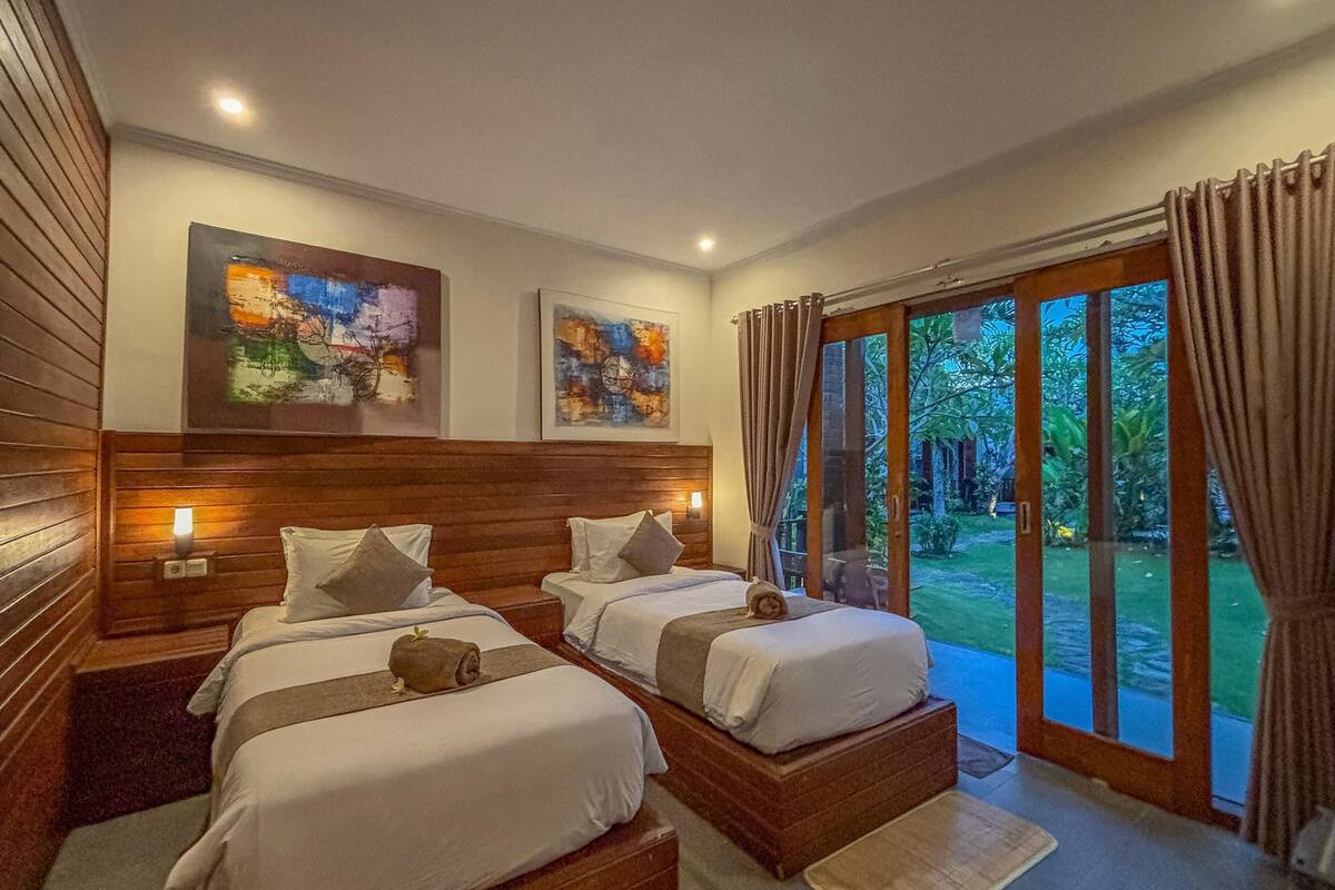 A bedroom with two beds, wooden headboards, and artwork on the walls.
