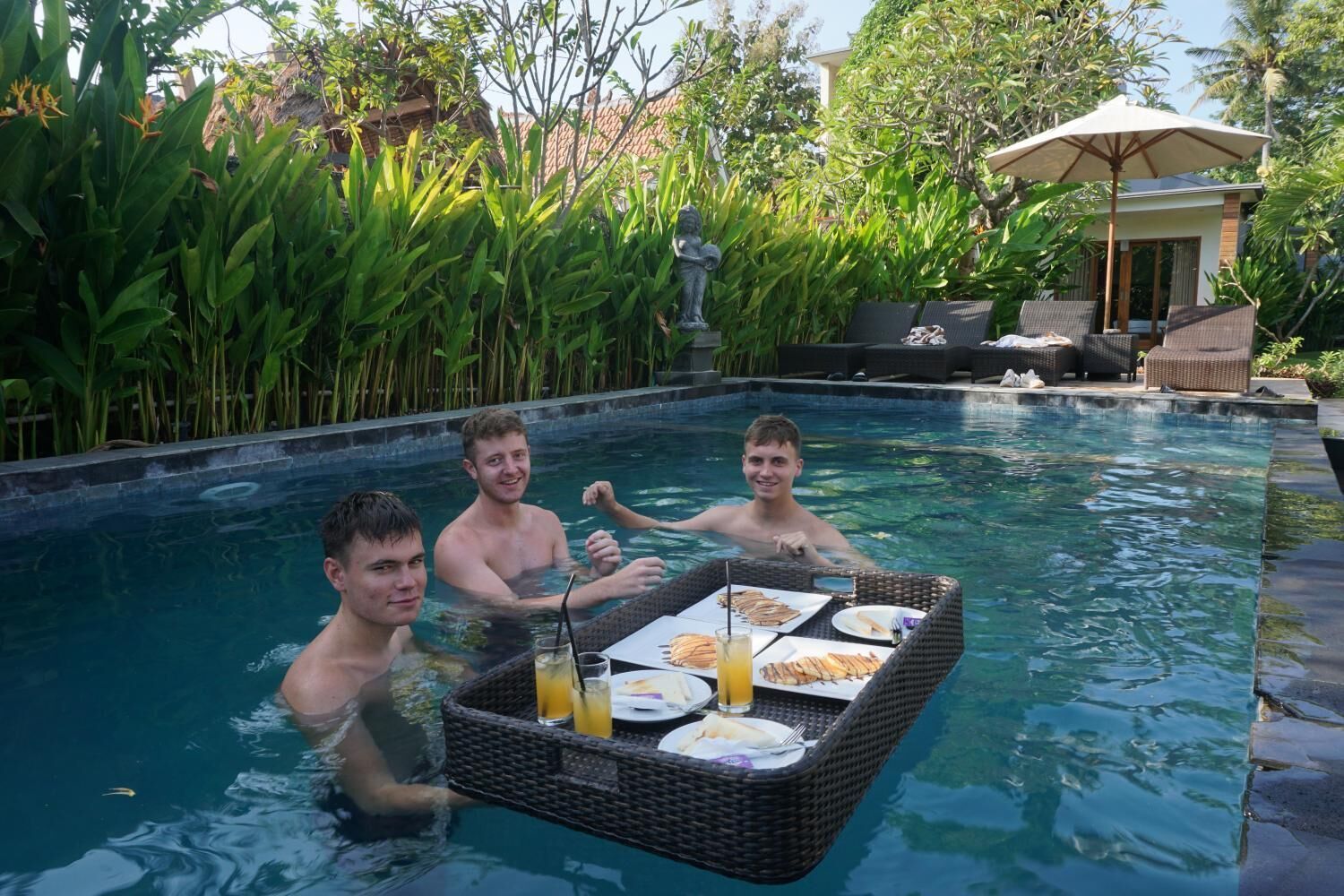 Un espace repas aménagé au bord de la piscine, avec une table dressée pour deux personnes, le tout entouré d’une végétation luxuriante.