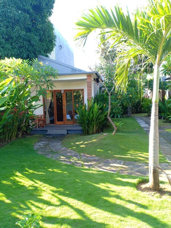 A house with a covered patio, a lawn, and various tropical plants.