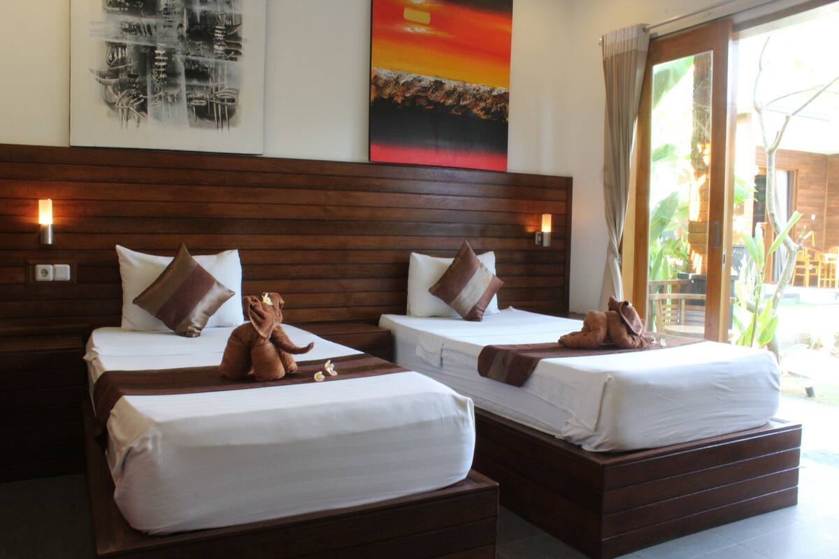 A hotel room with two beds, wooden headboards, and a view of the outdoors.