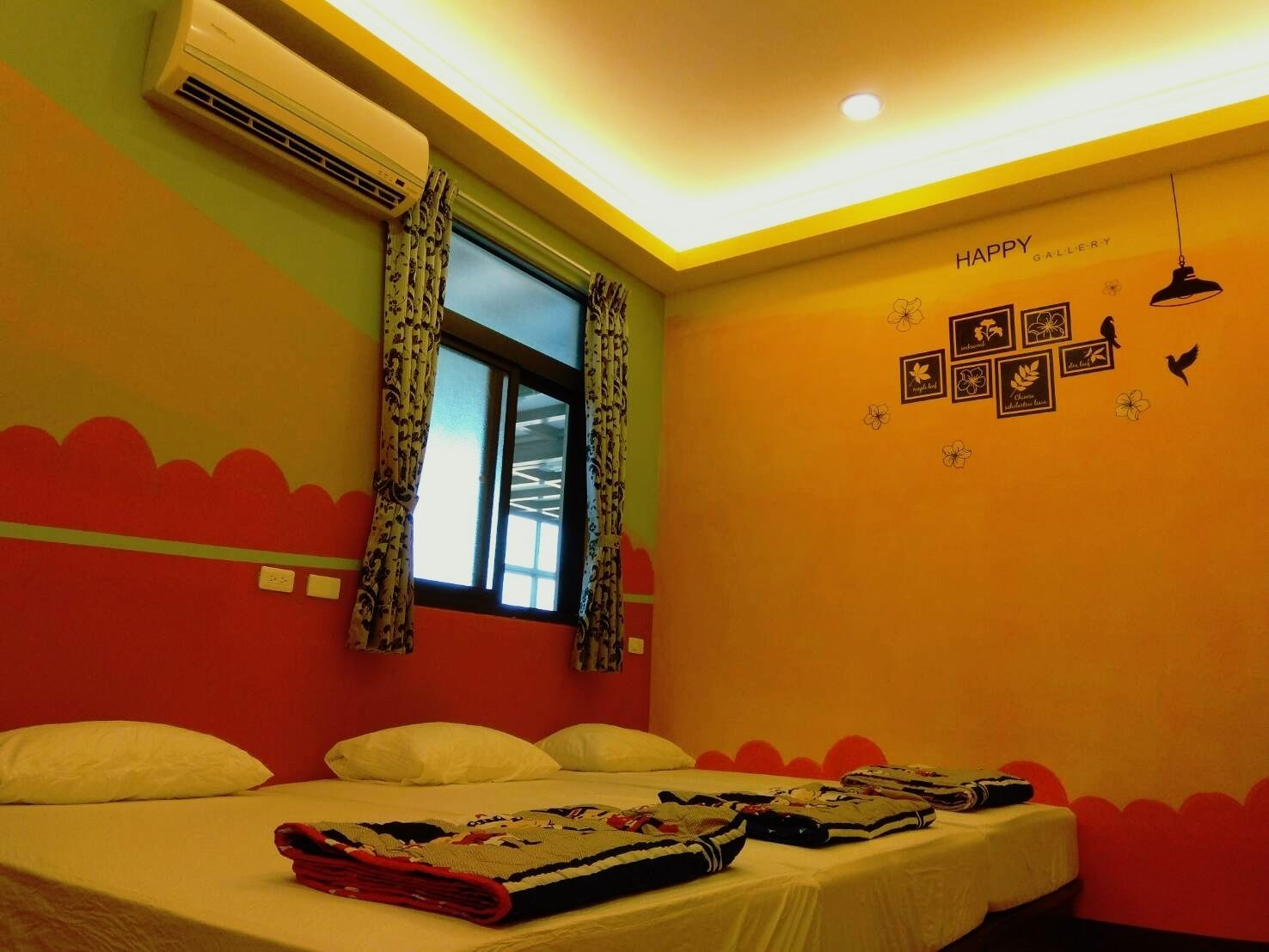 A room with a bed, air conditioning unit, window with curtains, and wall decorations including a 'Happy Gallery' sign.