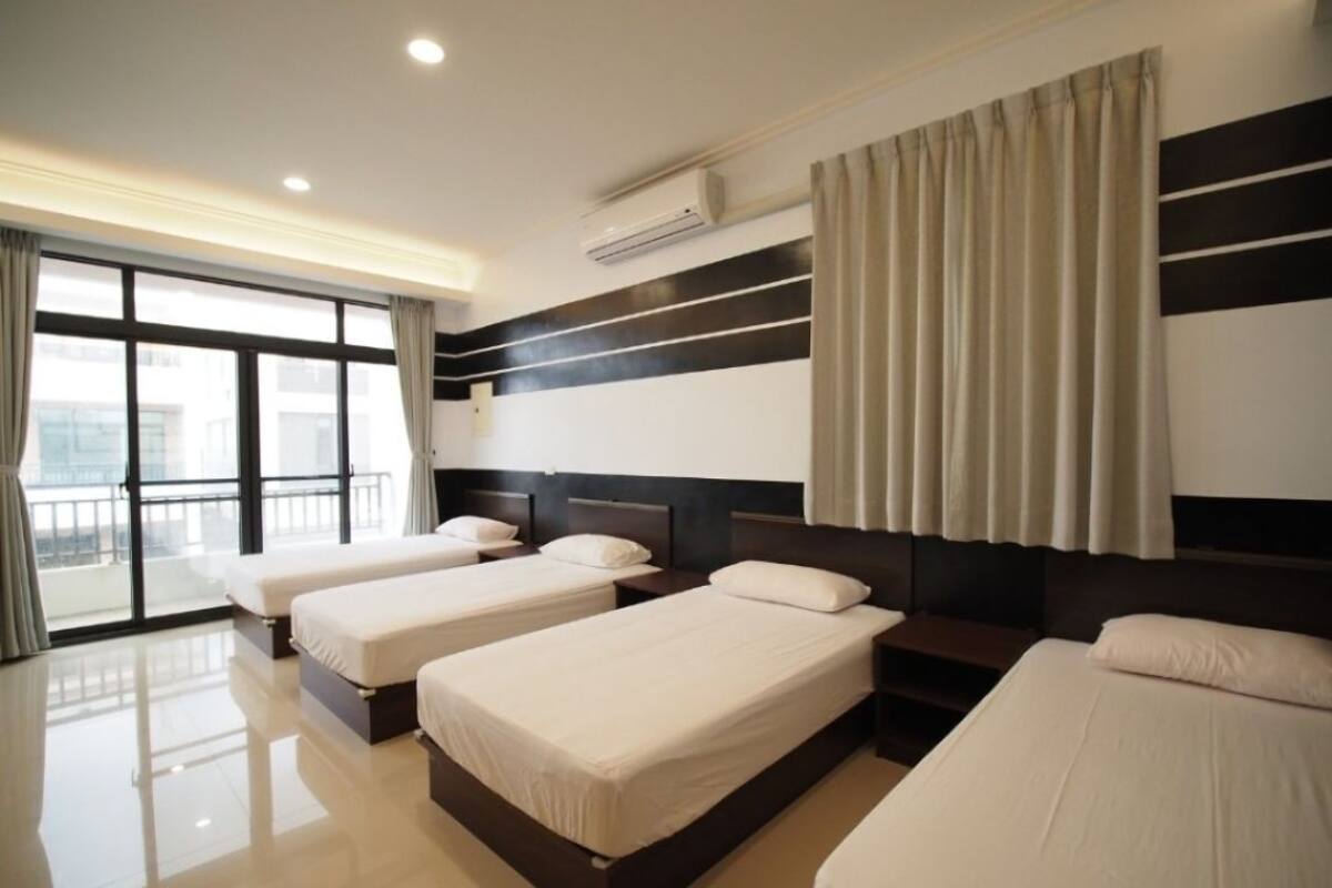 Habitación de hotel con tres camas individuales, un ventanal con cortinas, aire acondicionado y un balcón.