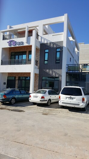 A modern building with a white facade and a black-tiled section. There are three cars parked in front. - Passion B&B (Magong)
