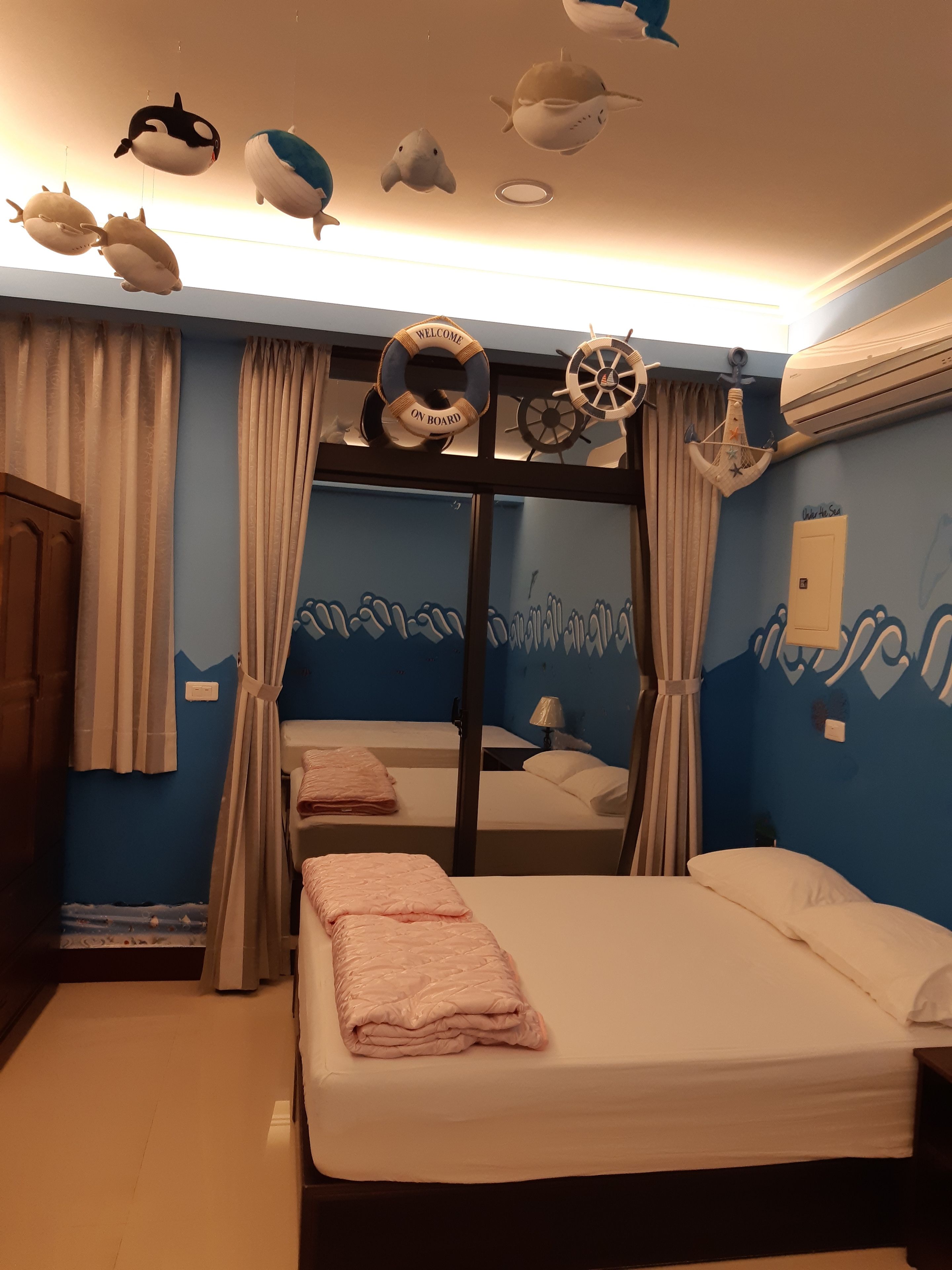 Quarto com duas camas, parede decorada com tema náutico e um boia salva-vidas.