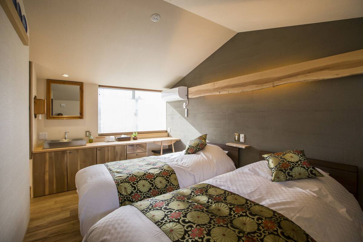 A bedroom with two beds, a desk, a window, and a mirror.