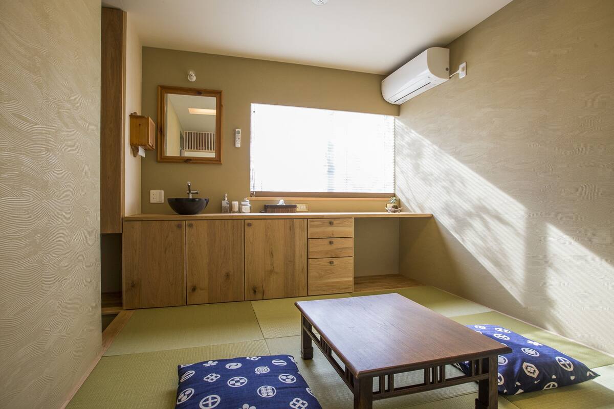 A traditional Japanese-style room with tatami flooring, a wooden table, a sink, and a window with blinds.