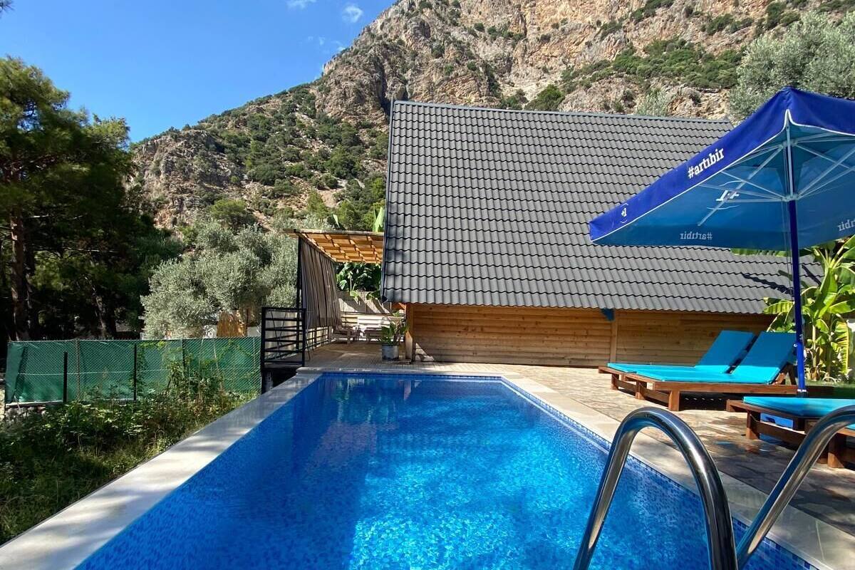 A swimming pool with a tiled deck, a wooden building with a tiled roof, and a mountain in the background.