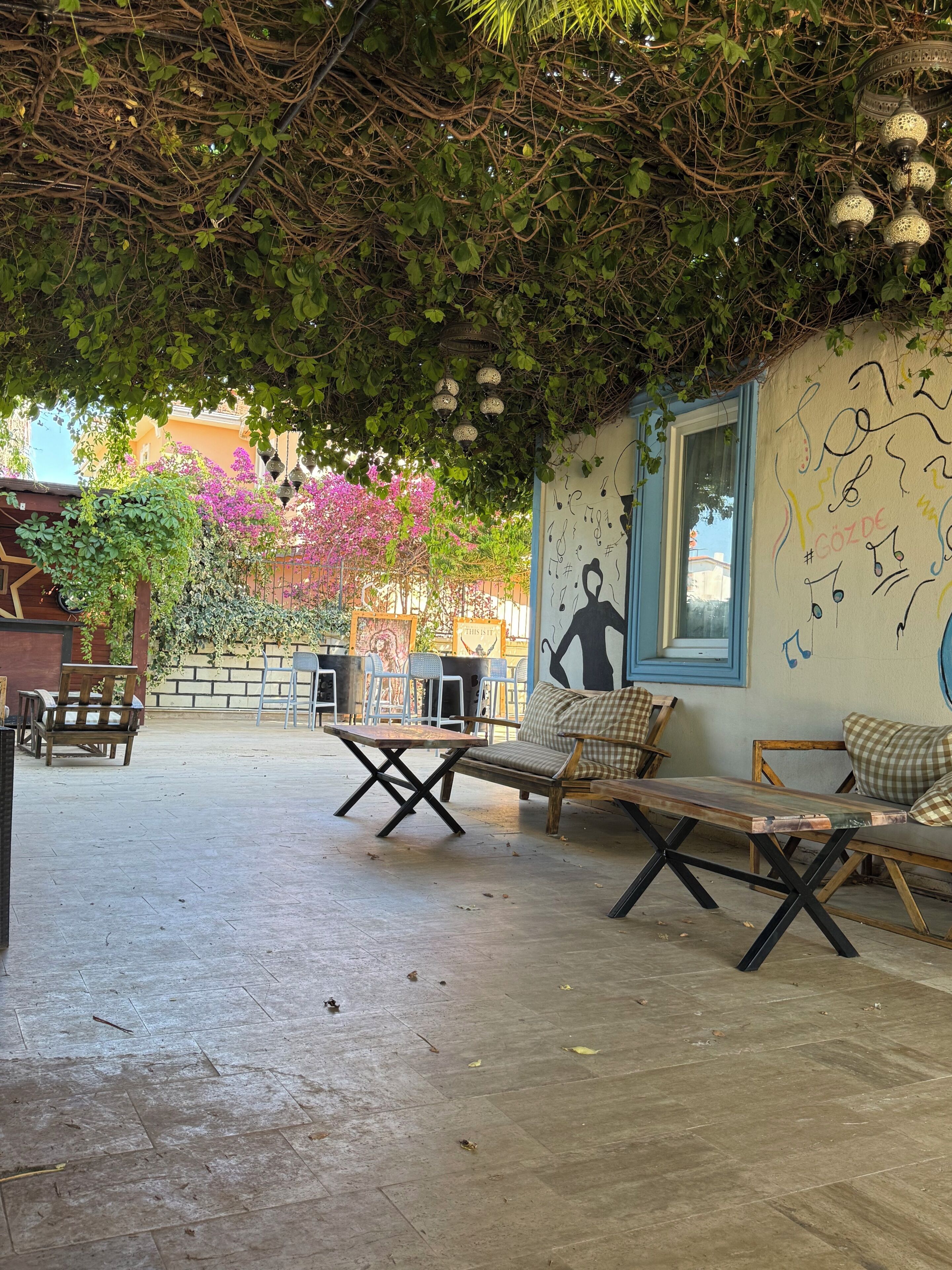An outdoor seating area with tables and chairs, a mural with musical notes, and a wall with a window.