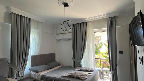 A modern hotel room with a large bed, a smaller bed, a sofa, a TV, and a balcony with a view. - Gozde Hotel (Serik)