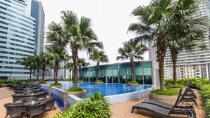 Area piscina sul tetto con poltrona prendisole, palme e moderni edifici sullo sfondo.